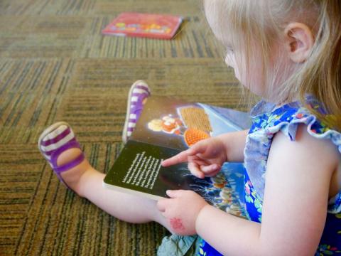 Toddler girl sitting in the library with open picture book on lap